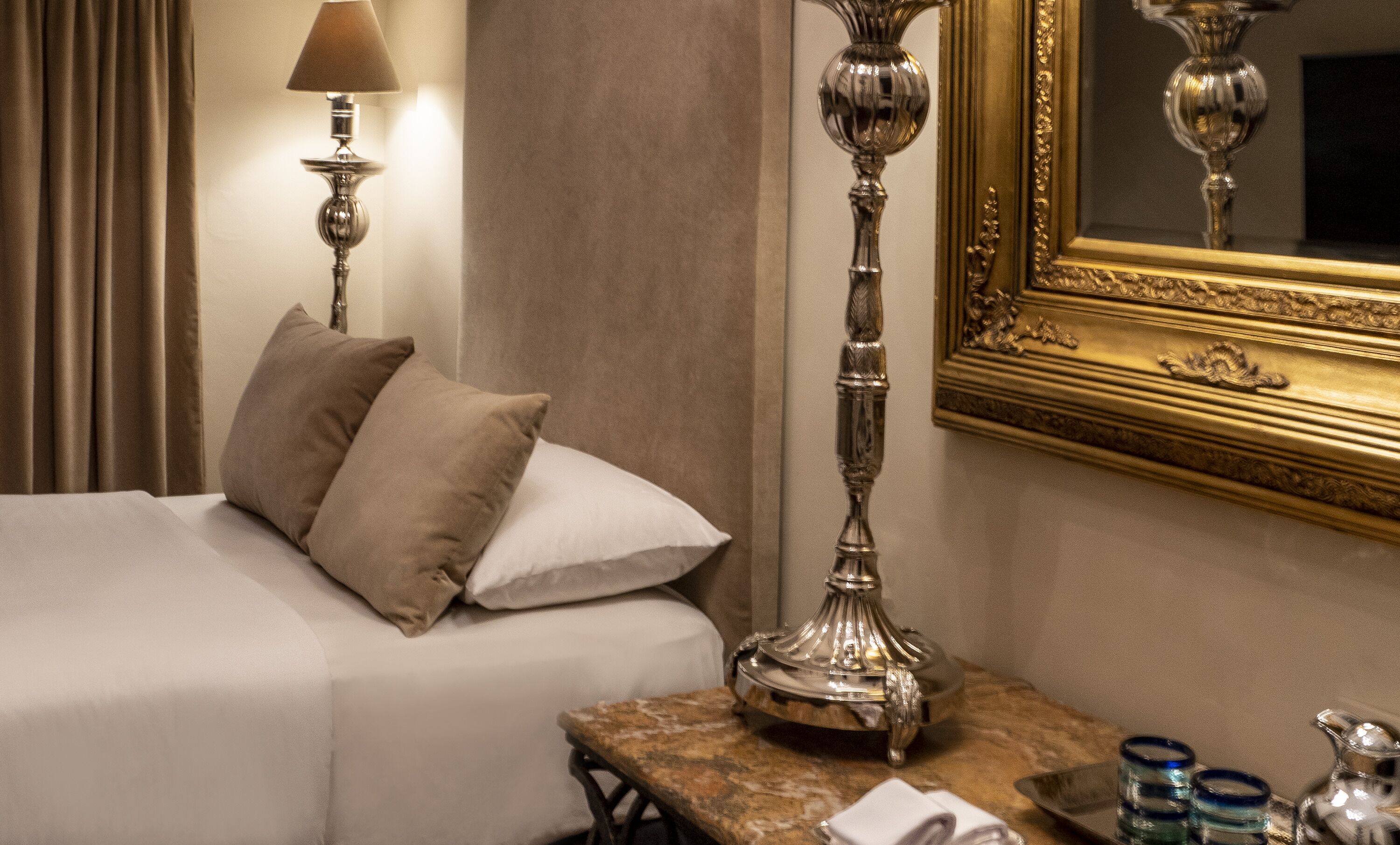 Habitación de hotel con cama, mesita de noche, lámpara, espejo y una mesa con bandeja.