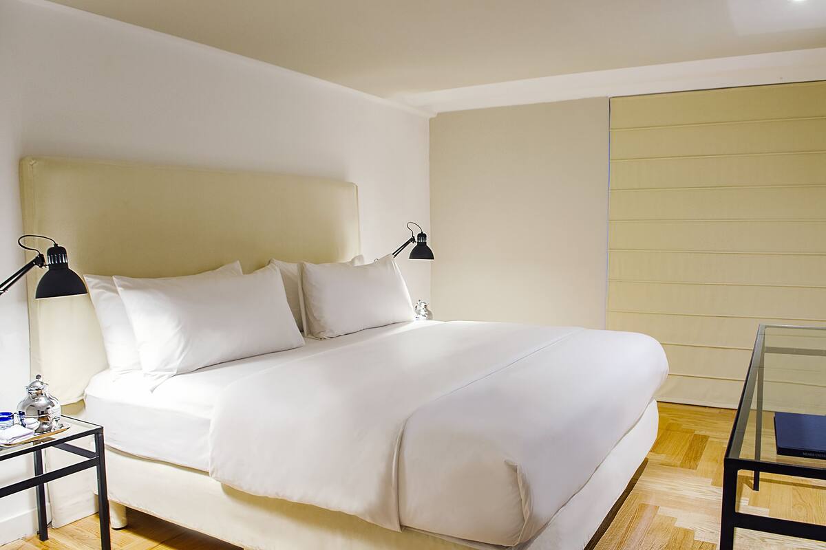 A neatly made bed with white bedding, two bedside lamps, and a glass coffee table.