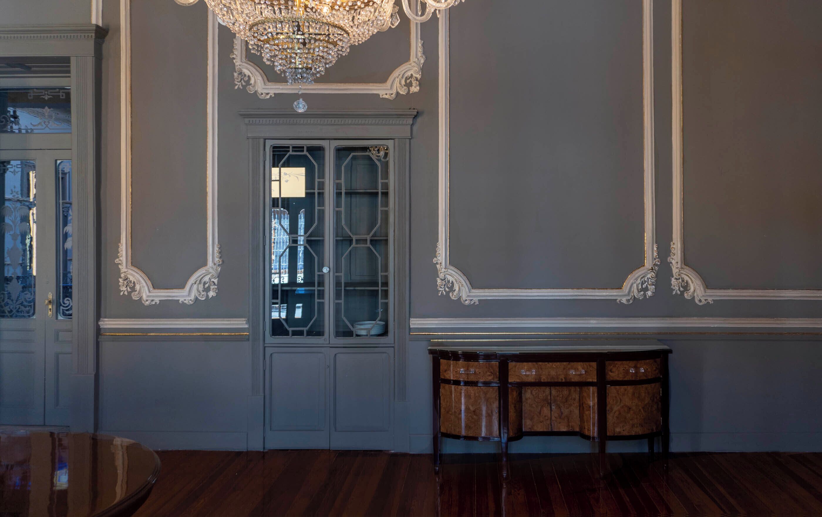 A room with a dark wooden floor, a glass cabinet with multiple shelves, and a decorative console table.
