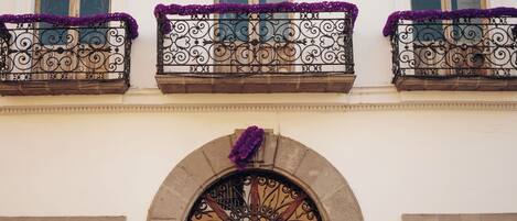 Une façade d’immeuble ornée de balcons en fer forgé ouvragé, décorés de fleurs violettes, avec une entrée centrale en arc de cercle et un portail en métal décoratif.
