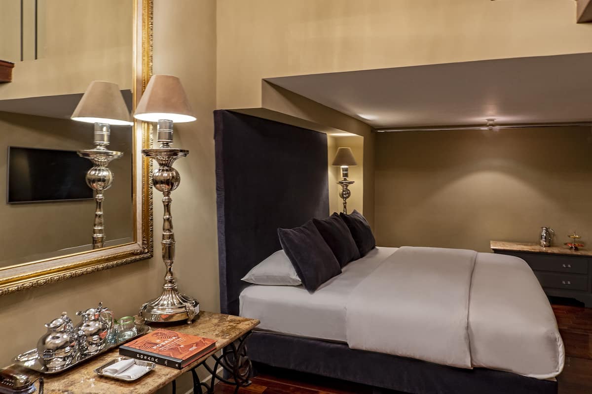 A hotel room with a large bed, a bedside table with a lamp, a mirror, and a TV.