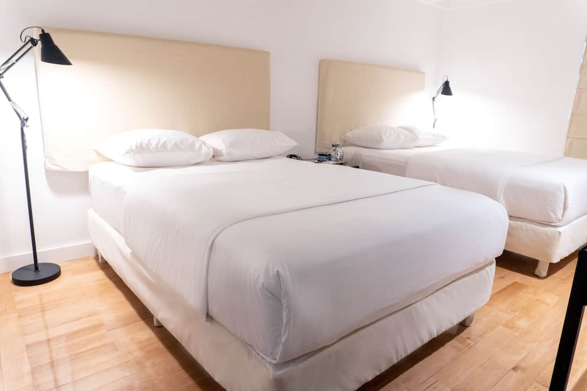 A hotel room with two beds, a bedside table, a lamp, and a wooden floor.