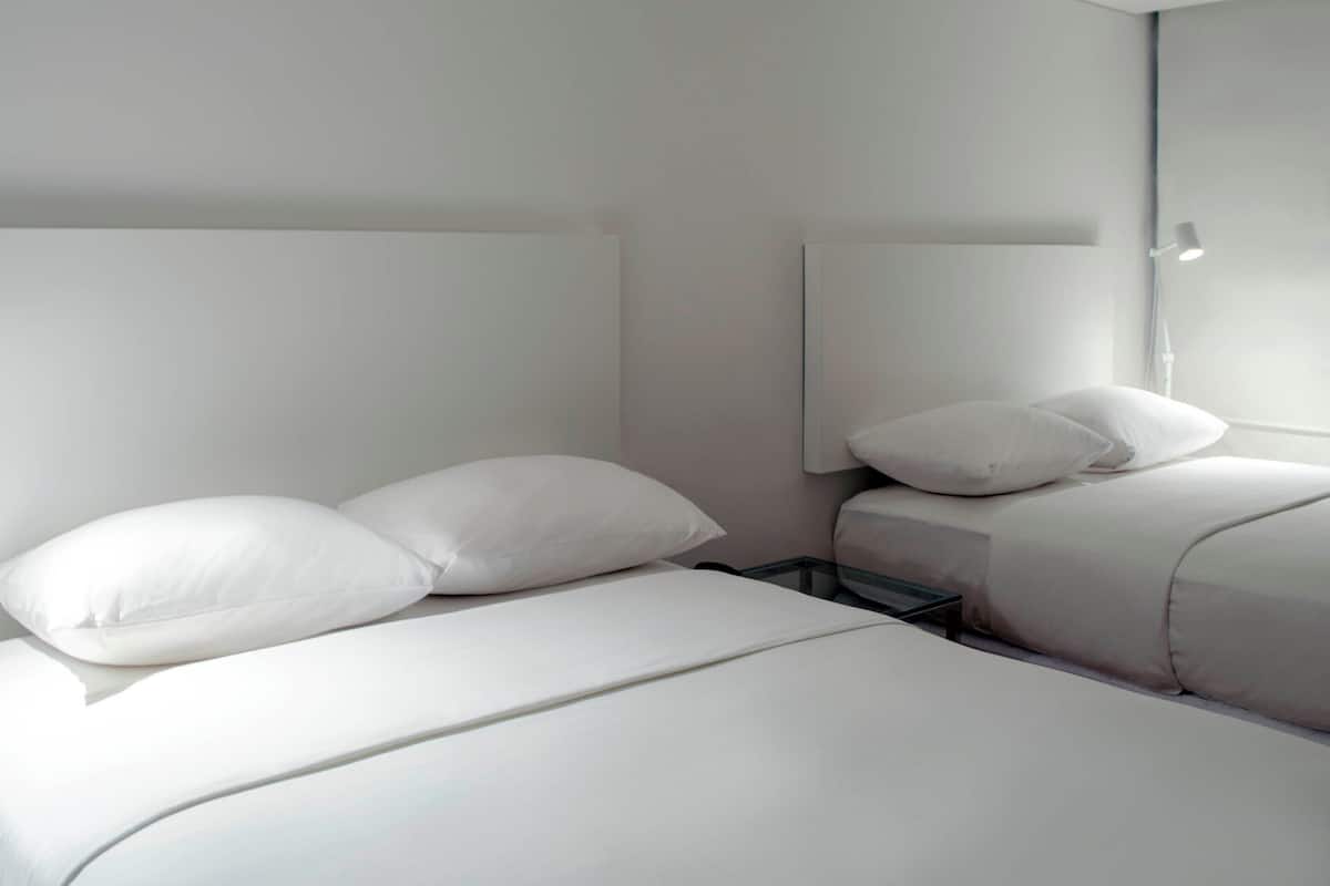 A modern hotel room with a large bed, two pillows, a bedside table, and a wall-mounted lamp.