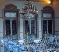 Un candelabro con múltiples niveles y luces que imitan velas, paneles de pared ornamentados y una barandilla metálica con detalles azules.