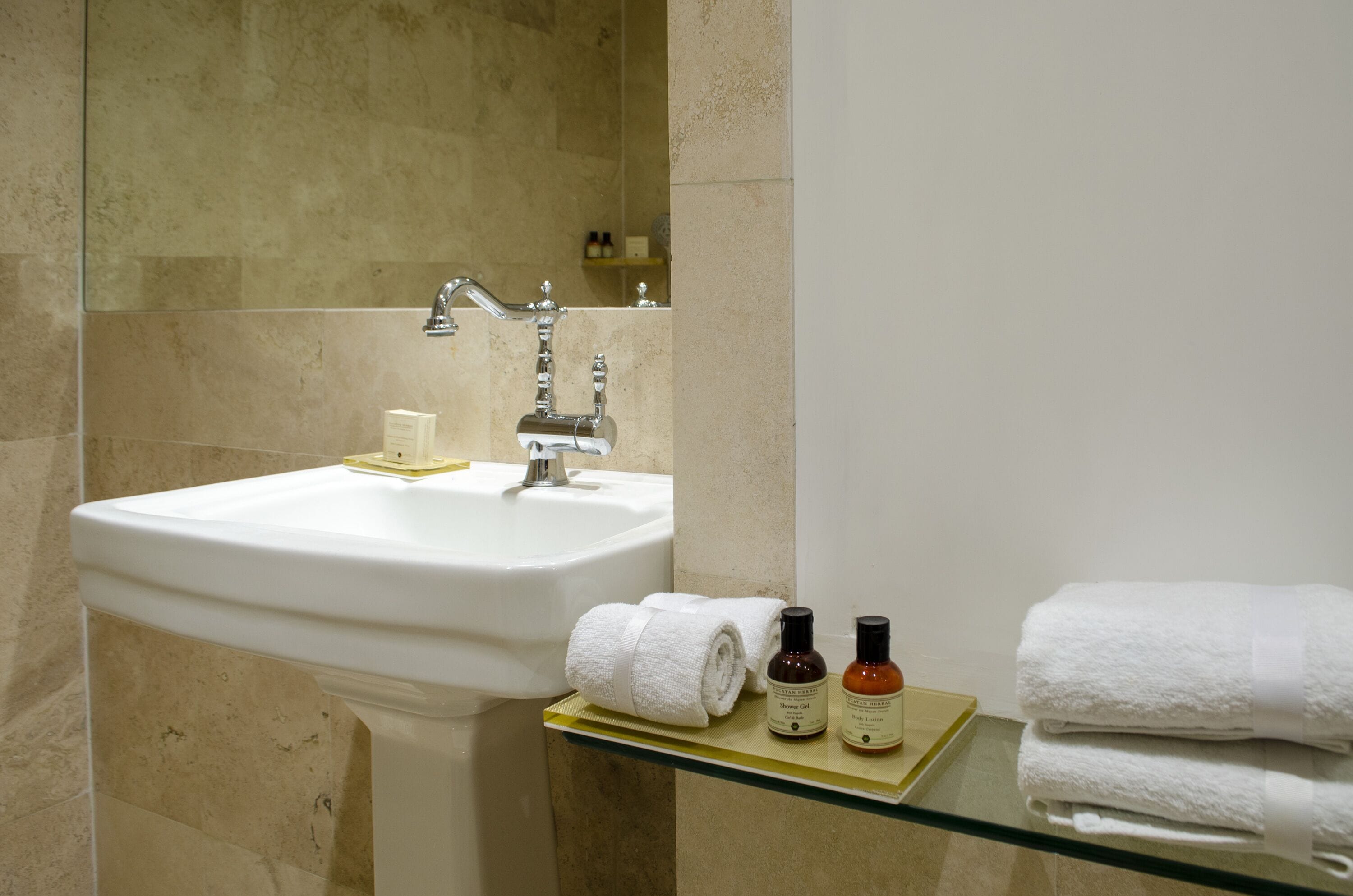 Een badkamer met een wit wastafelmeubel, een spiegel en een glazen plank met handdoeken en toiletartikelen.