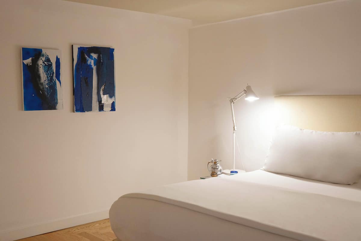 A bedroom with a bed, a nightstand, a lamp, and two abstract paintings on the wall.
