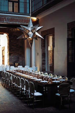 Una larga mesa de comedor dispuesta para una comida en una habitación con paredes de ladrillo y una lámpara de araña con forma de estrella.