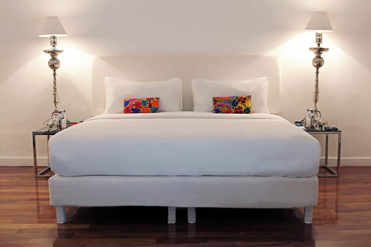 A large bed with white bedding, two bedside tables with lamps, and colorful pillows.