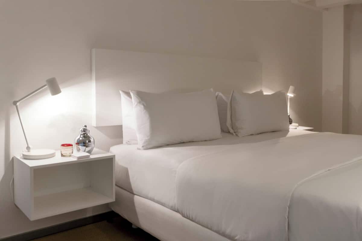 A neatly made bed with white linens and pillows, a bedside table with a lamp, and a small decorative item.