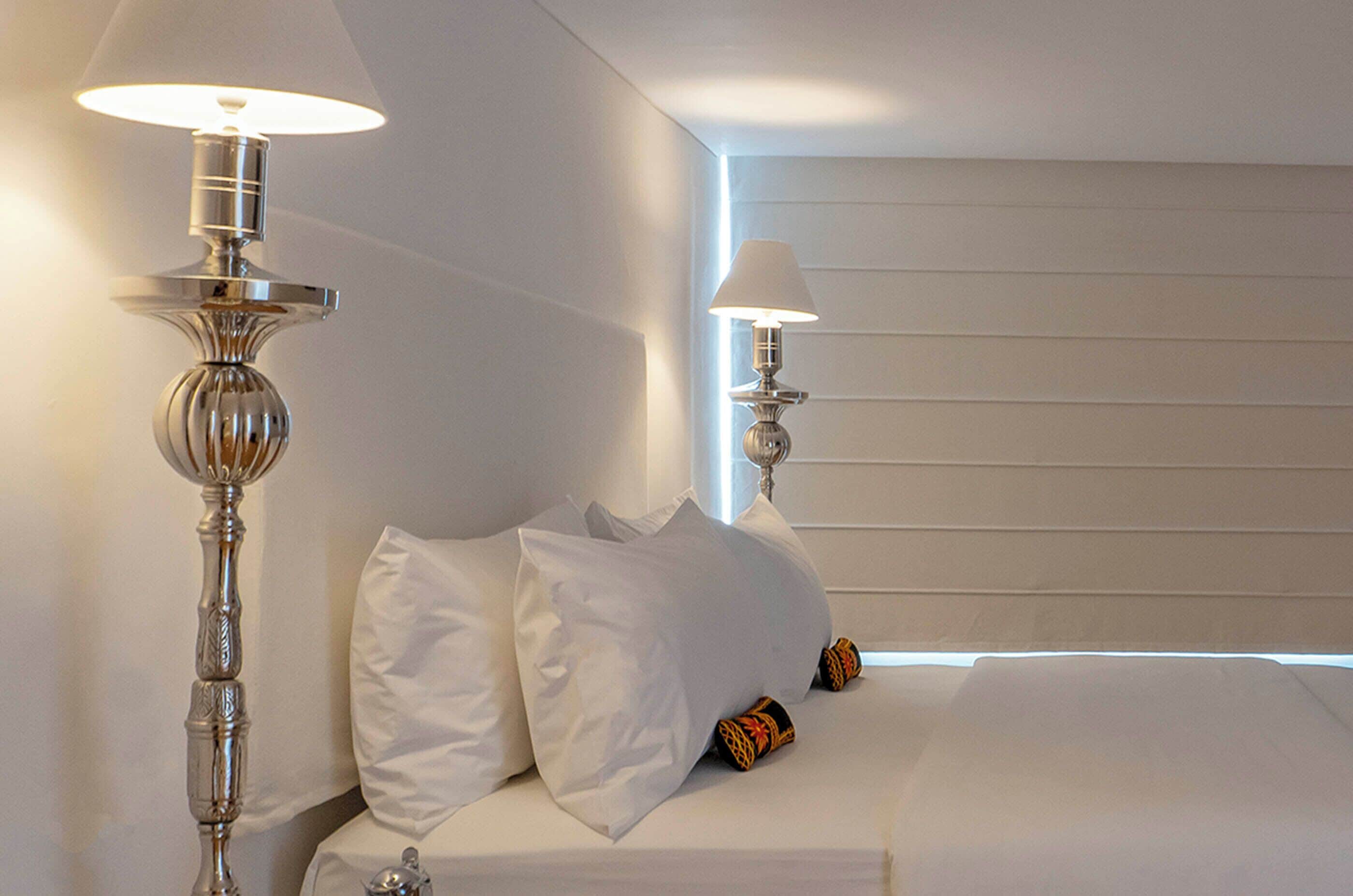 A hotel room with a neatly made bed, two bedside lamps, and a wall with horizontal lines.