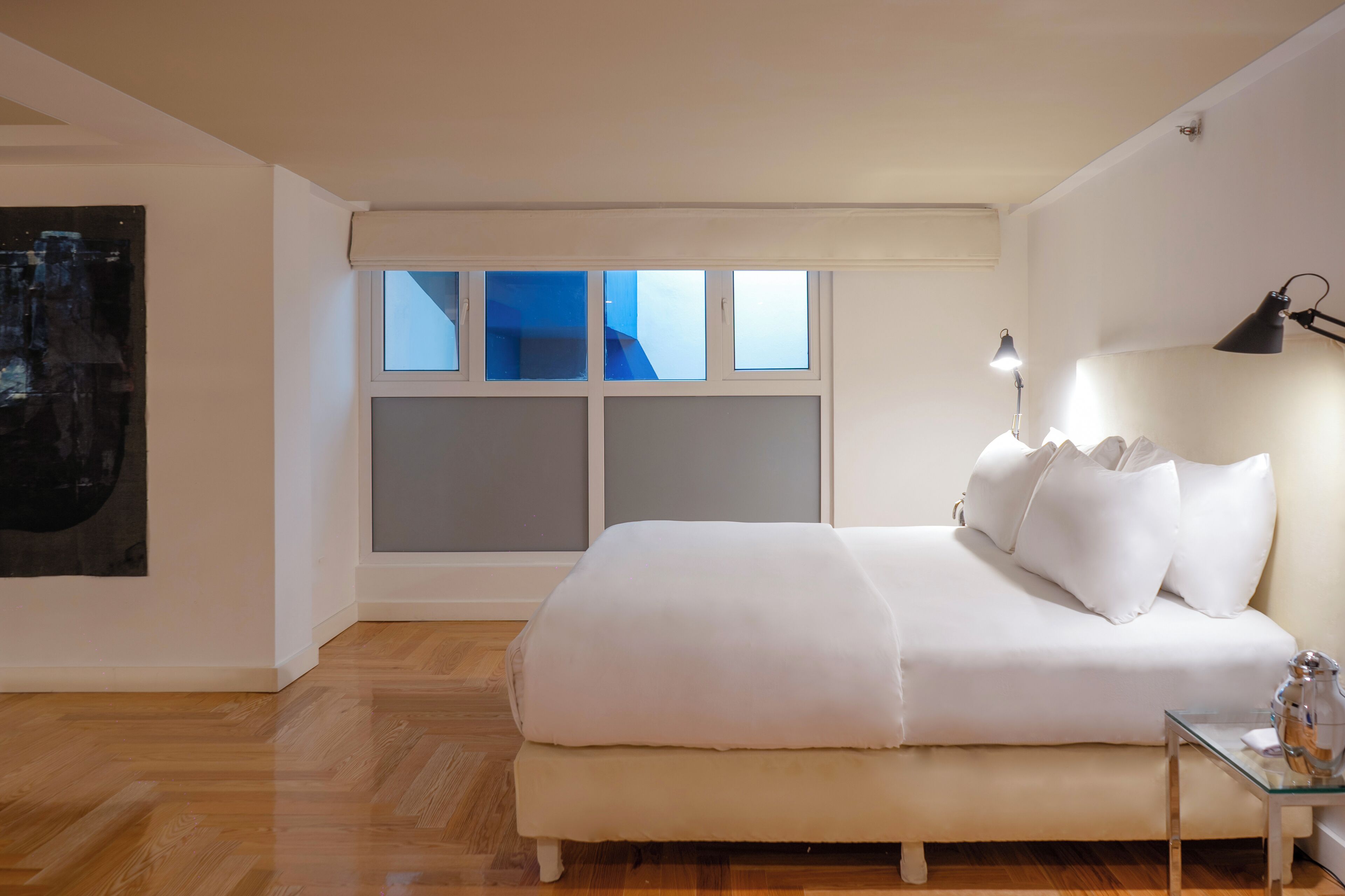 Een slaapkamer met een groot bed, een nachtkastje, een lamp en een raam met jaloezieën.