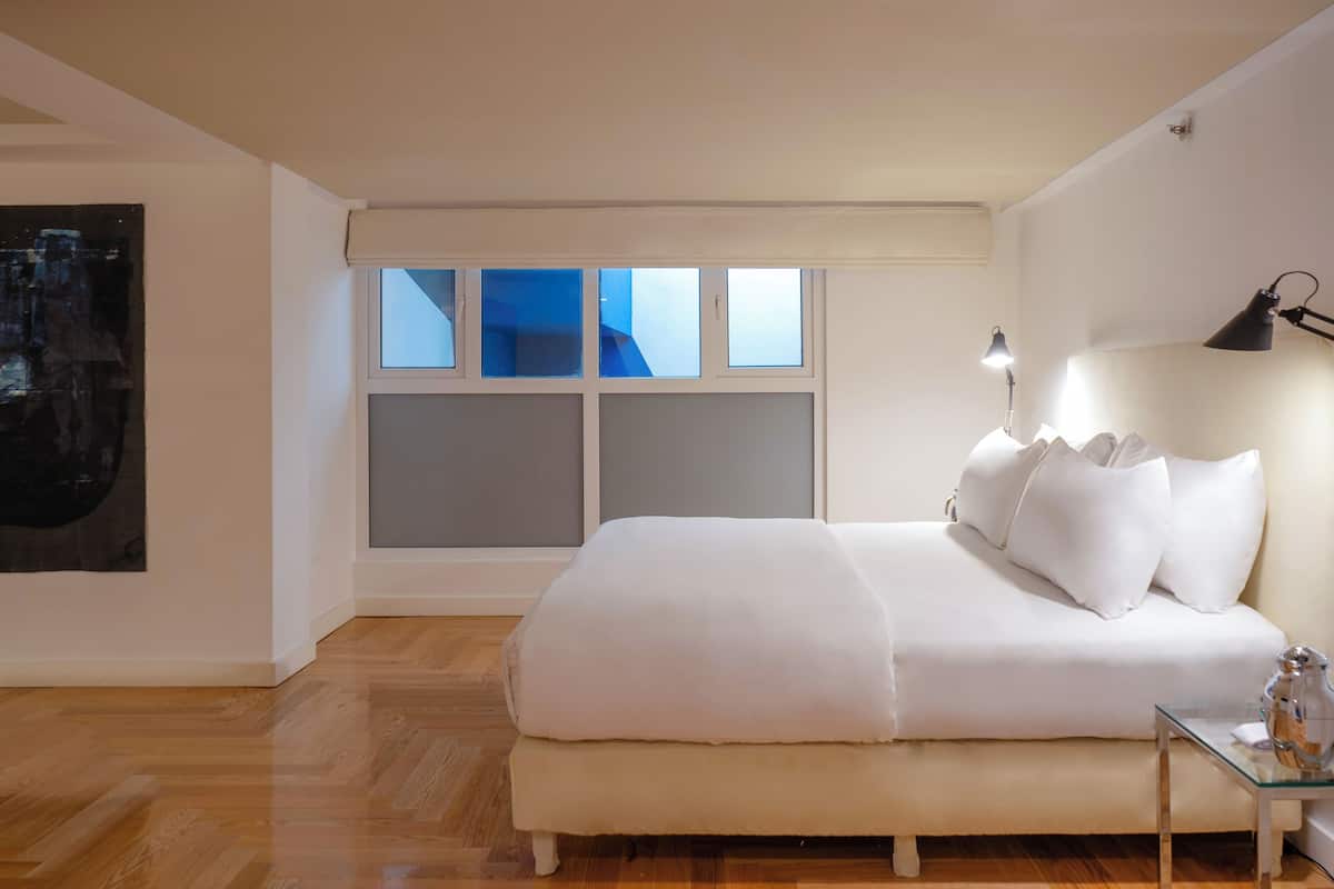 Une chambre à coucher avec un grand lit, une table de chevet, une lampe et une fenêtre avec des stores.