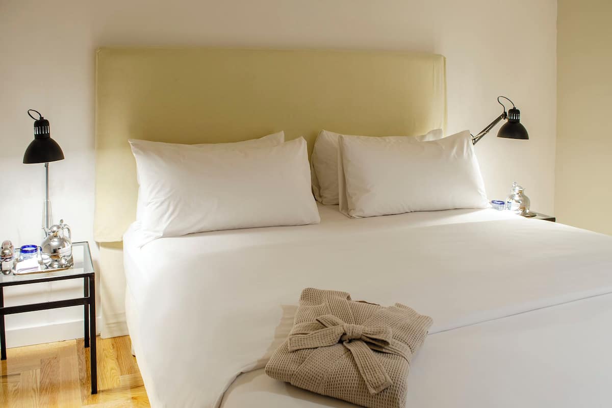 Une chambre d’hôtel avec un grand lit, deux lampes de chevet, une table de chevet avec une lampe et une serviette pliée posée sur le lit.