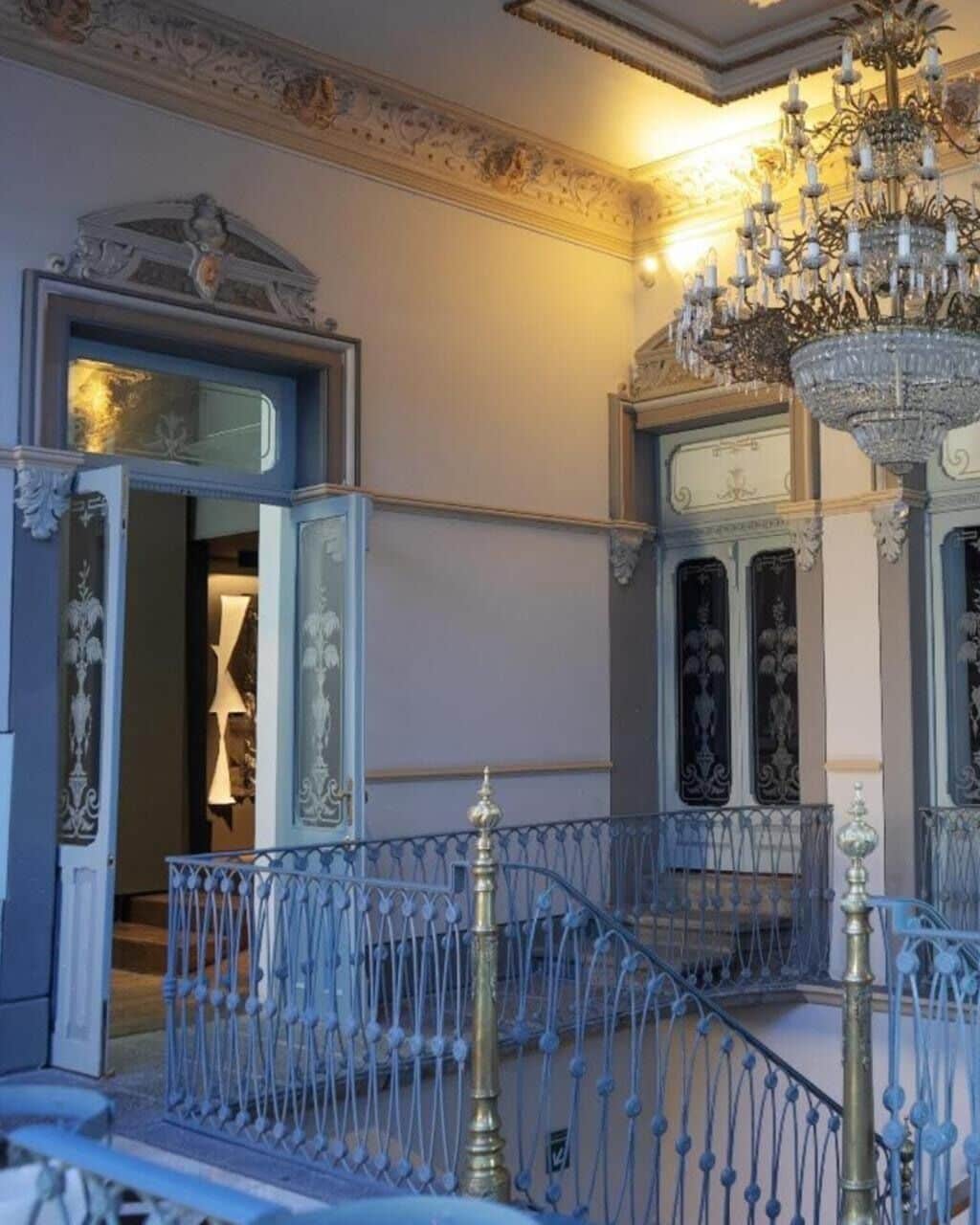 Un salón imponente con barandillas de metal decoradas, un candelabro y un espejo grande.