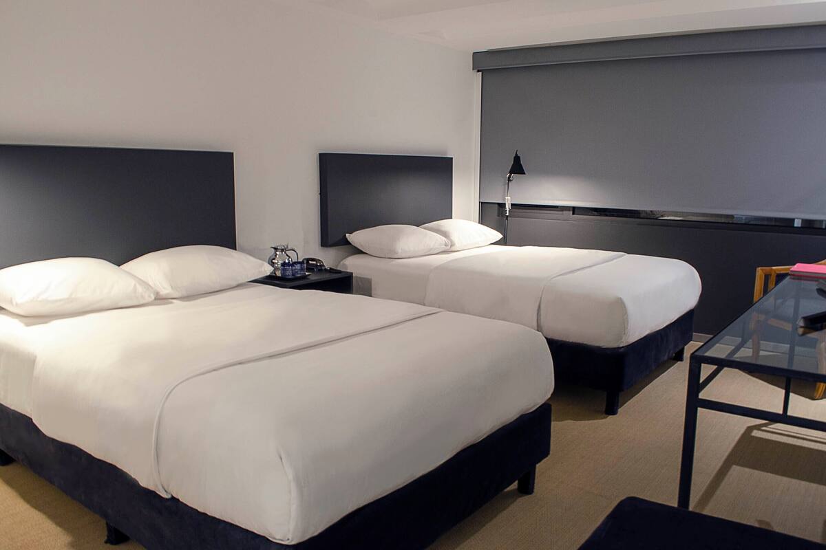A hotel room with two beds, a desk, and a lamp.