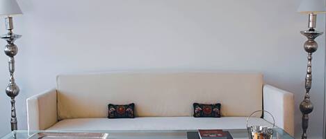 Una sala de estar moderna con una mesa de centro de vidrio, un sofá blanco con cojines estampados y dos lámparas de pie decorativas.