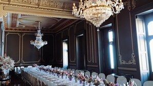 Uma longa mesa de banquete montada para um evento formal, com lustres ornamentados e arranjos florais.