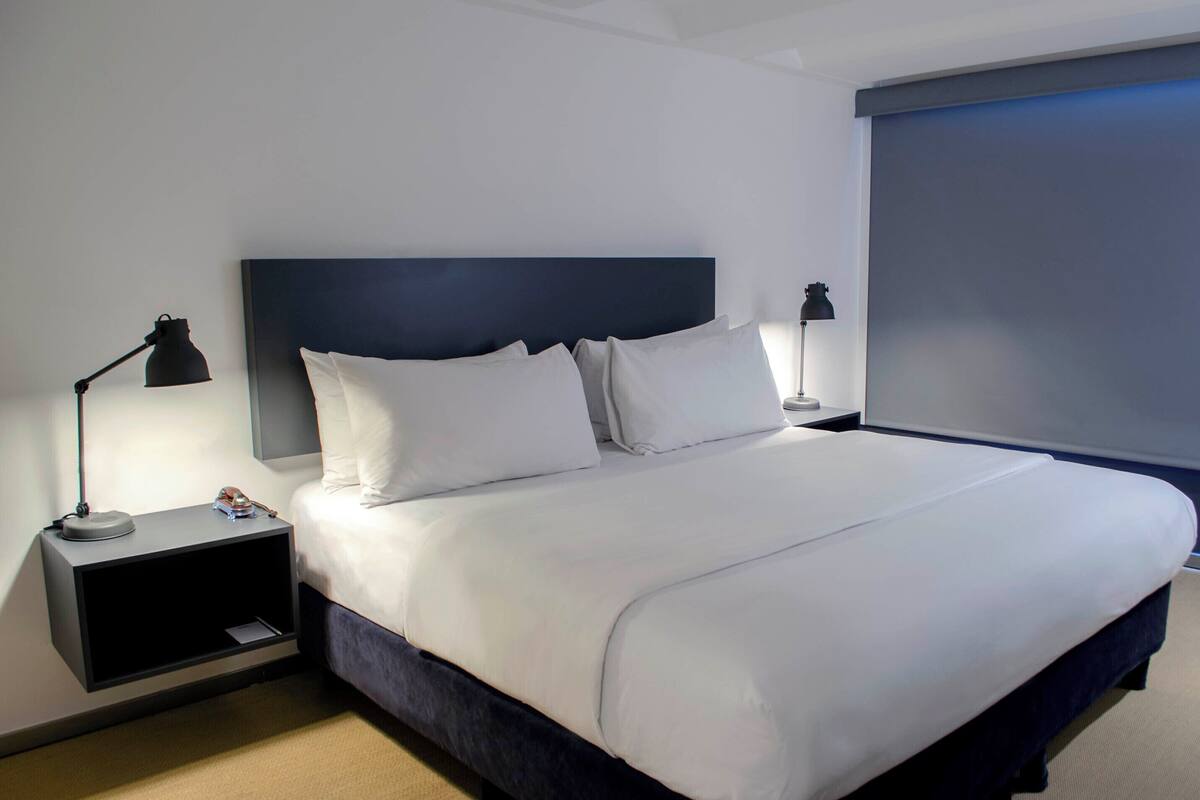 A neatly made bed with white linens, a dark headboard, and two bedside lamps.