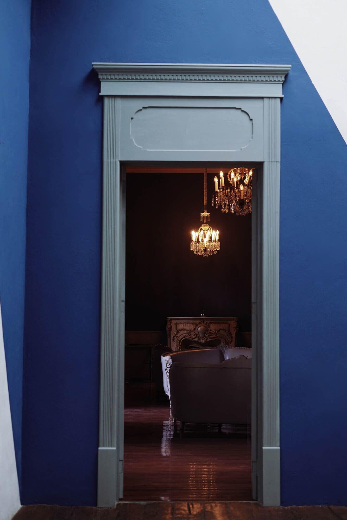 Une porte donnant sur une chambre à coucher, où l’on aperçoit un lustre et un lit.