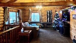 A log cabin interior with a cozy living area, a wooden ceiling, a Christmas tree, and a television. - Beautiful Log Cabin 11ac. 4 br. 2.5 ba. on snowmobile trails in Manistee forest. (Township of Branch)