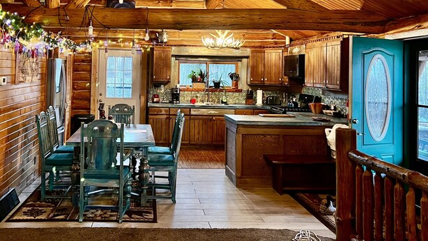 A rustic cabin interior with a wooden dining area, a kitchen with wooden cabinets, and a large island. - Beautiful Log Cabin 11ac. 4 br. 2.5 ba. on snowmobile trails in Manistee forest. (Township of Branch)
