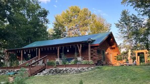 A log cabin with a covered porch, stone steps, and a small garden area. - Beautiful Log Cabin 11ac. 4 br. 2.5 ba. on snowmobile trails in Manistee forest. (Township of Branch)