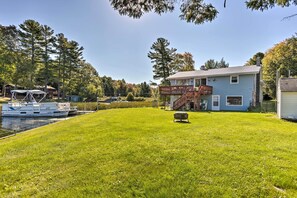 A house with a deck, a boat docked by the water, and a grassy yard. - Lakefront Ludington Retreat w/ Kayaks & Fire Pit! (Ludington)