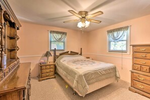 A bedroom with a bed, wooden dresser, nightstand, and a ceiling fan. - Lakefront Ludington Retreat w/ Kayaks & Fire Pit! (Ludington)