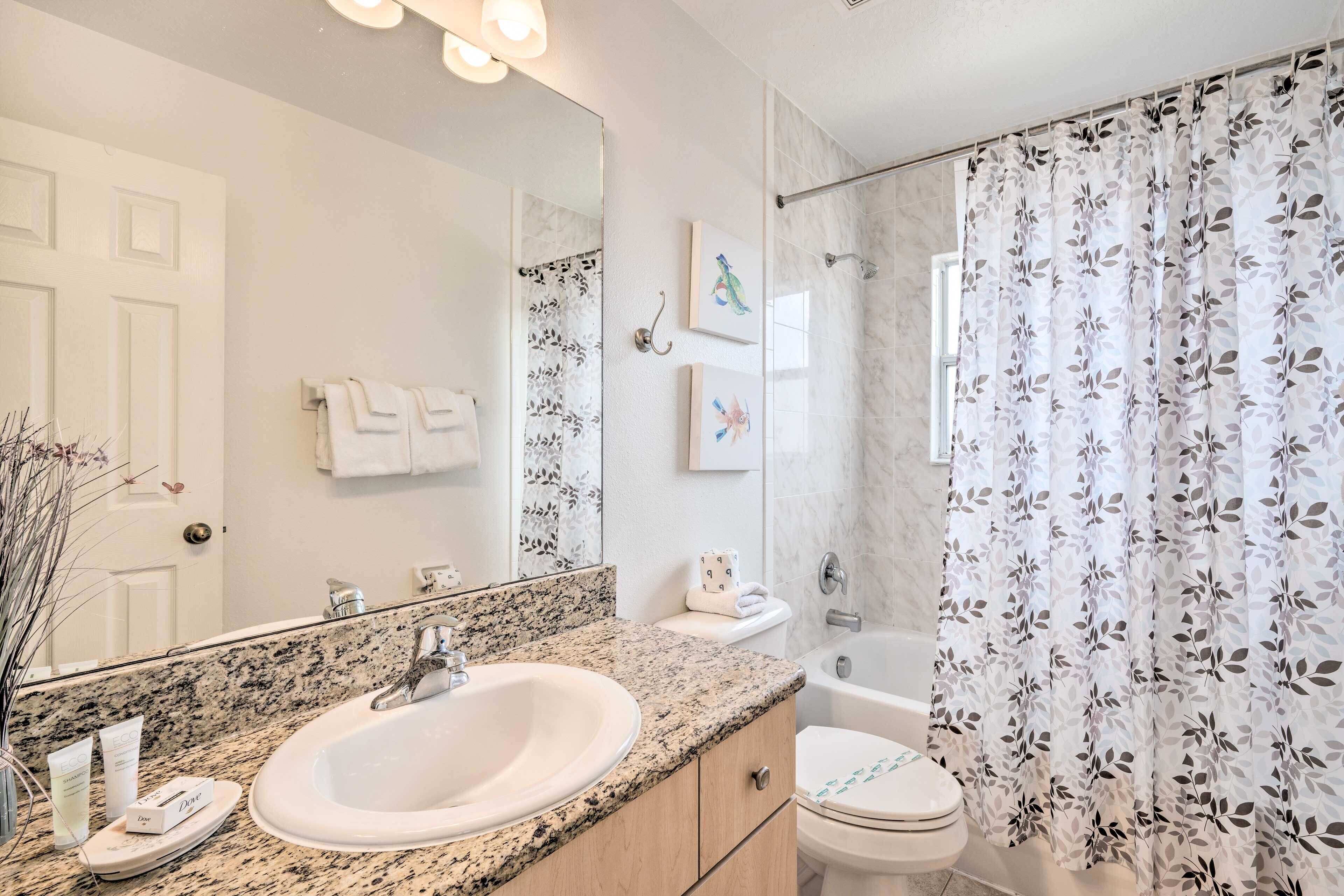 A bathroom with a granite countertop sink, a mirror, a toilet, and a shower curtain with a leaf pattern.