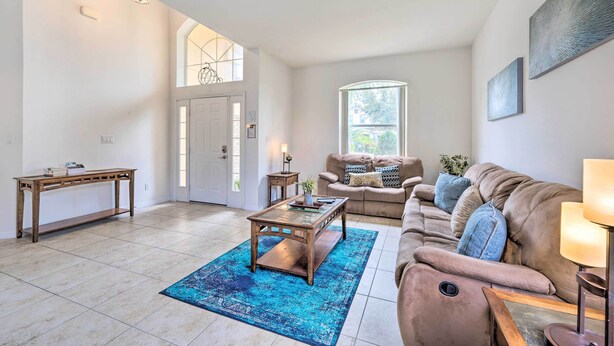 A spacious living room with a large window, a sofa, a coffee table, and a console table. - Dog-Friendly Kissimmee Home w/ Lanai + Pool! (Kissimmee)