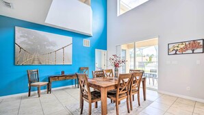 A dining area with a wooden table and chairs, a blue accent wall, and a large window. - Dog-Friendly Kissimmee Home w/ Lanai + Pool! (Kissimmee)