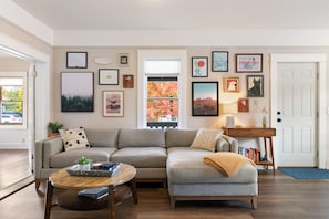 A living room with a grey sectional sofa, a round wooden coffee table, and a bookshelf.