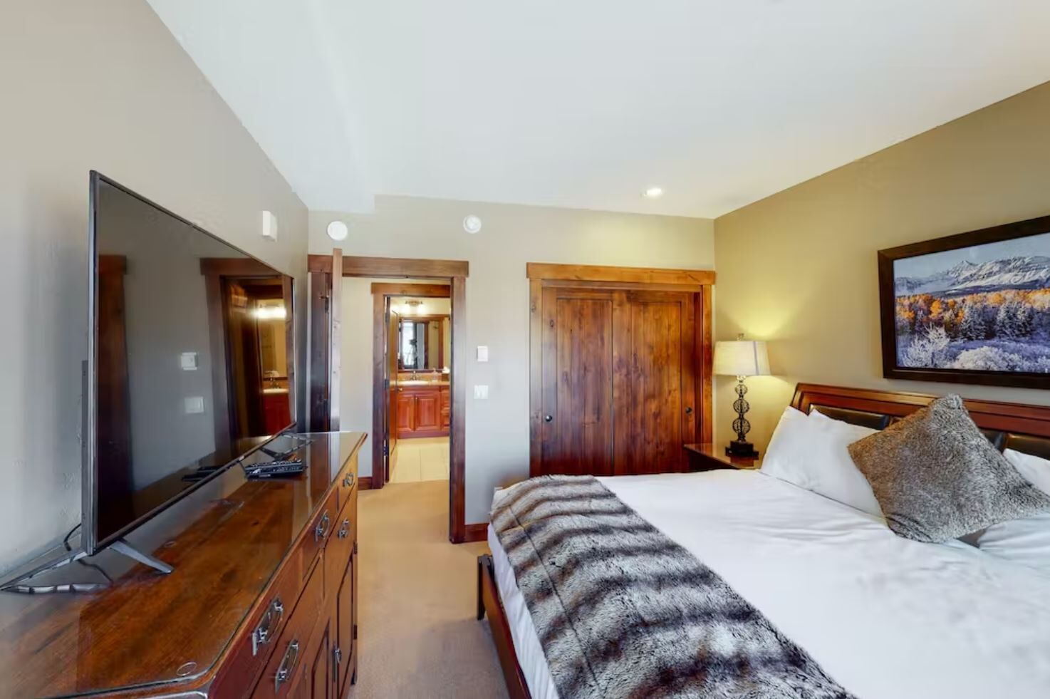 Une chambre d’hôtel dotée d’une grande télévision à écran plat, d’un lit recouvert d’une couverture à motifs, d’une armoire en bois, d’un bureau avec une lampe et d’un tableau accroché au mur.