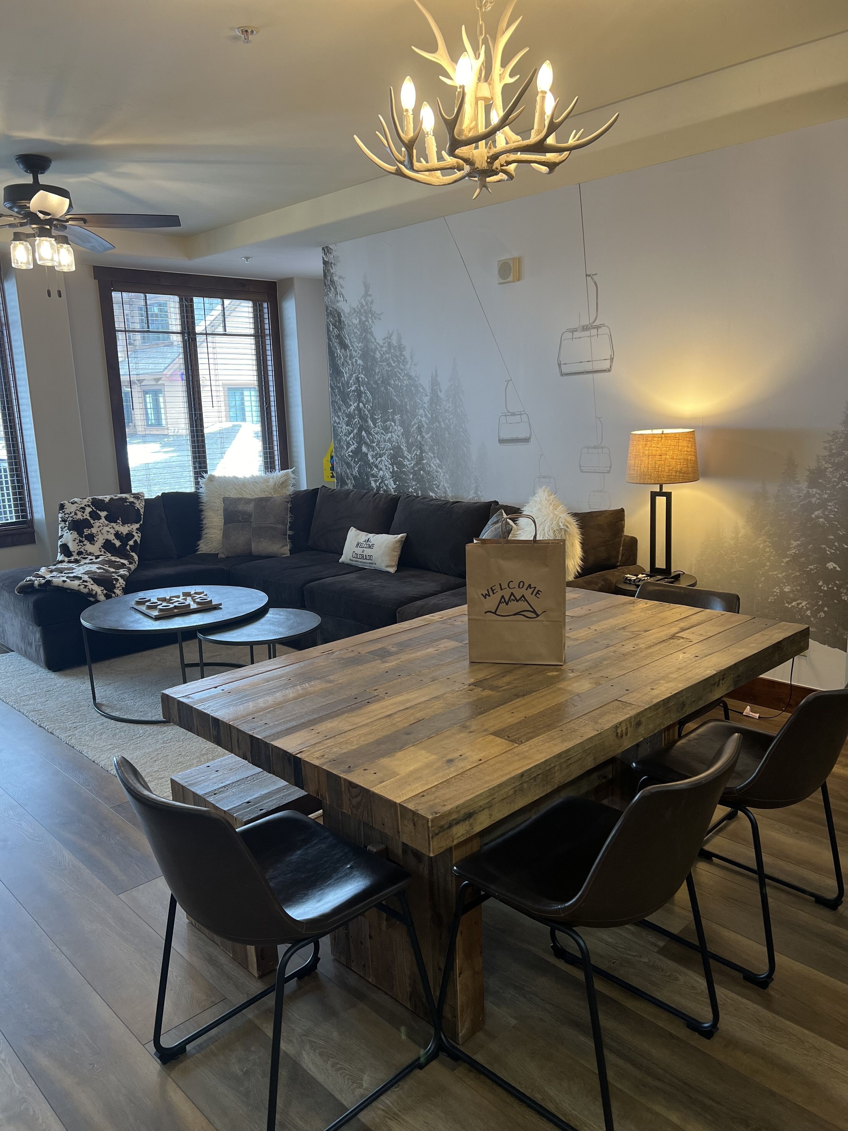 Ein modernes Wohnzimmer mit einem Holzesstisch, schwarzen Stühlen, einem schwarzen Sofa und einer Kronleuchter.