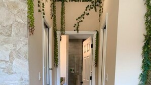 A hallway with a stone wall on one side, wooden flooring, and a door at the end leading to a bathroom. - 🌿Welcome to the Jungle🌿 (Davenport)