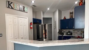 A kitchen with a marble countertop, blue cabinets, and wooden stools. - 🌿Welcome to the Jungle🌿 (Davenport)