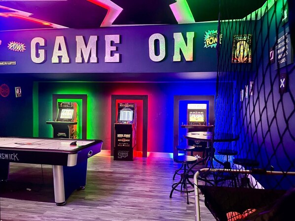 Une salle de jeux équipée d’une table de billard, de jeux d  ’arcade et d’un éclairage néon.