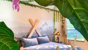 A bedroom with a bed, a nightstand, a lamp, and a wall mural. - 🌿Welcome to the Jungle🌿 (Davenport)