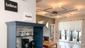 A modern living room with a dark blue cabinet, a coffee maker, and a wooden coffee table. There are two framed pictures on the wall and a sign that says "believe inspire". - 🌿Welcome to the Jungle🌿 (Davenport)