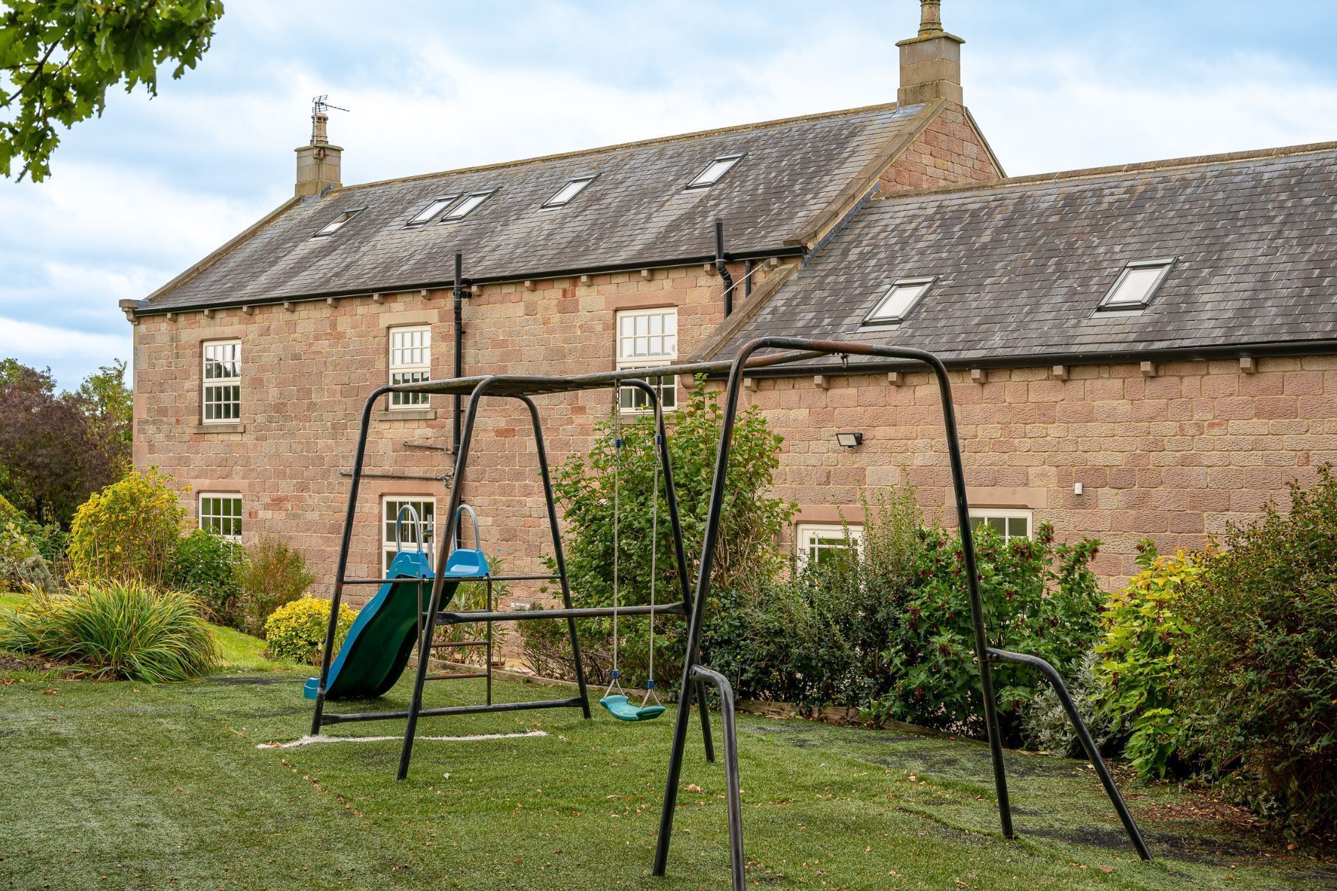 A stone building with a grassy yard, a swing set, and a slide.