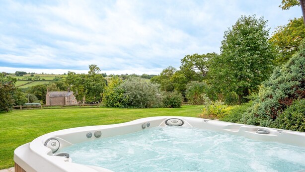 Un bain à remous dans un jardin luxuriant, avec vue sur un paysage rural.