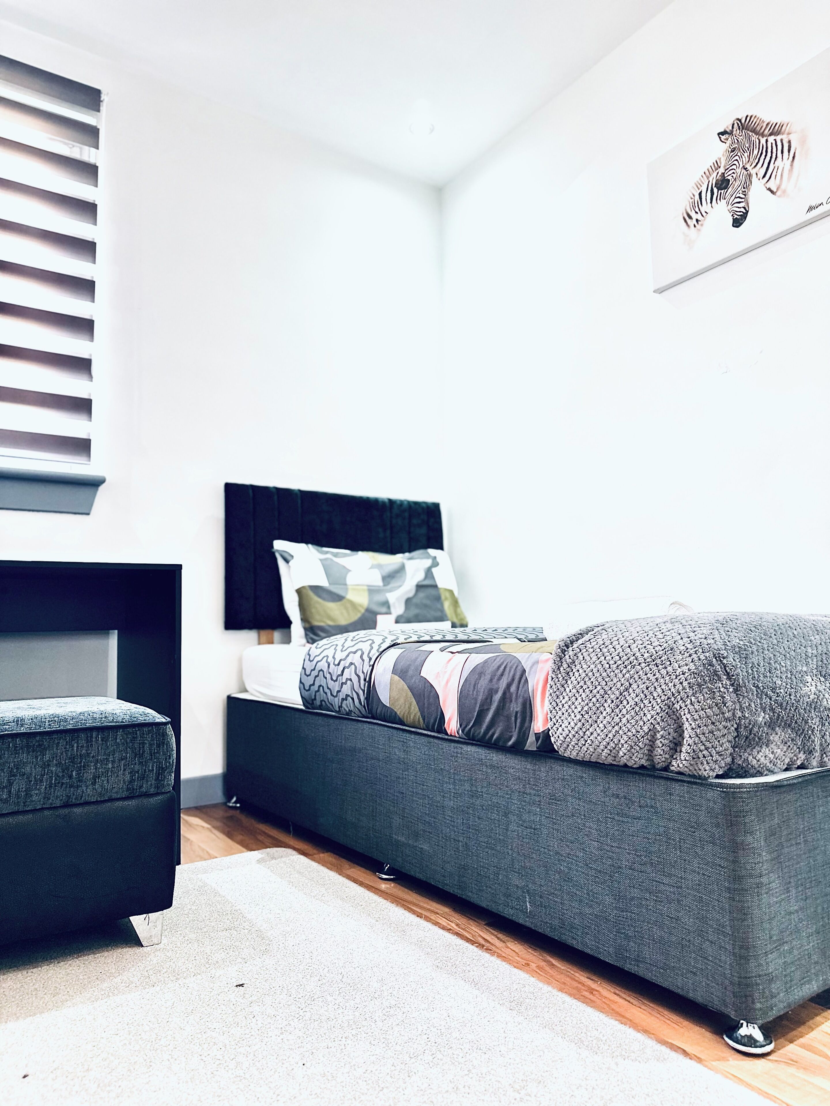 Un dormitorio moderno con un sofá cama gris, una mesita de noche pequeña y un estante fijado a la pared.