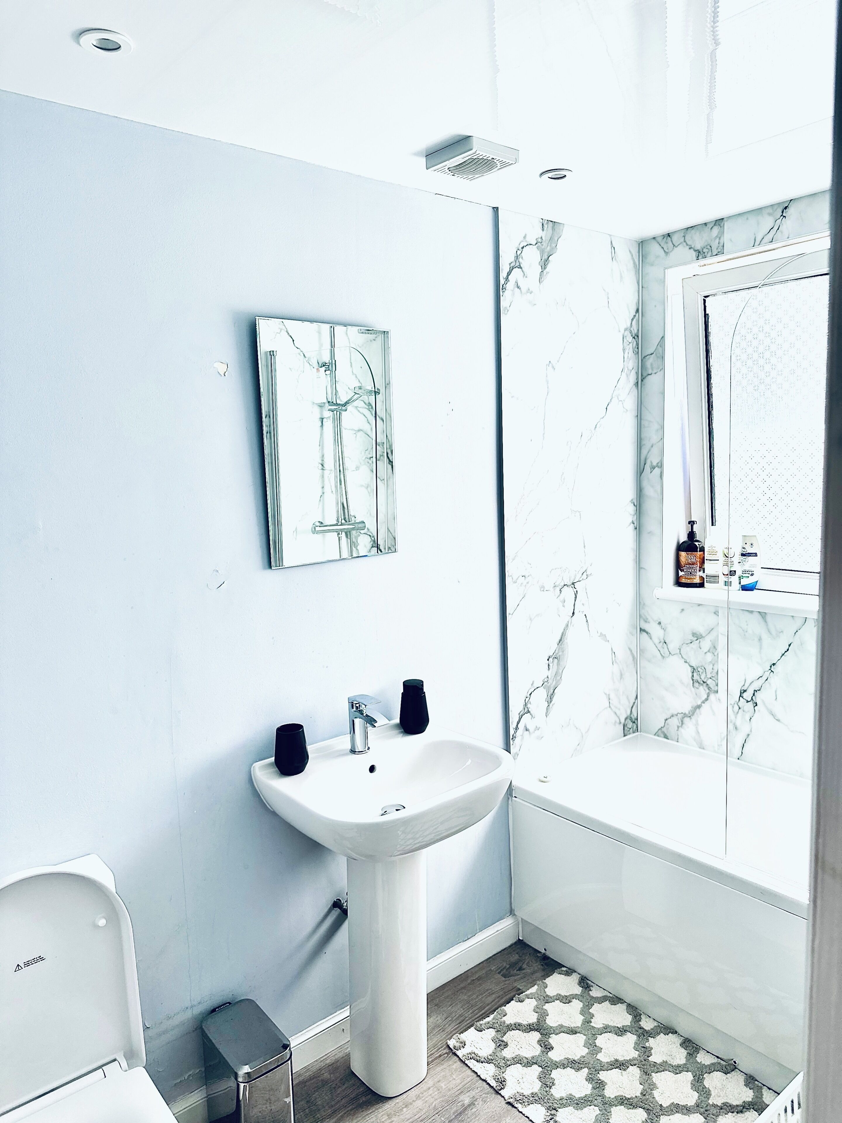 Un bagno con un lavandino bianco, uno specchio, una doccia e una parete in marmo.