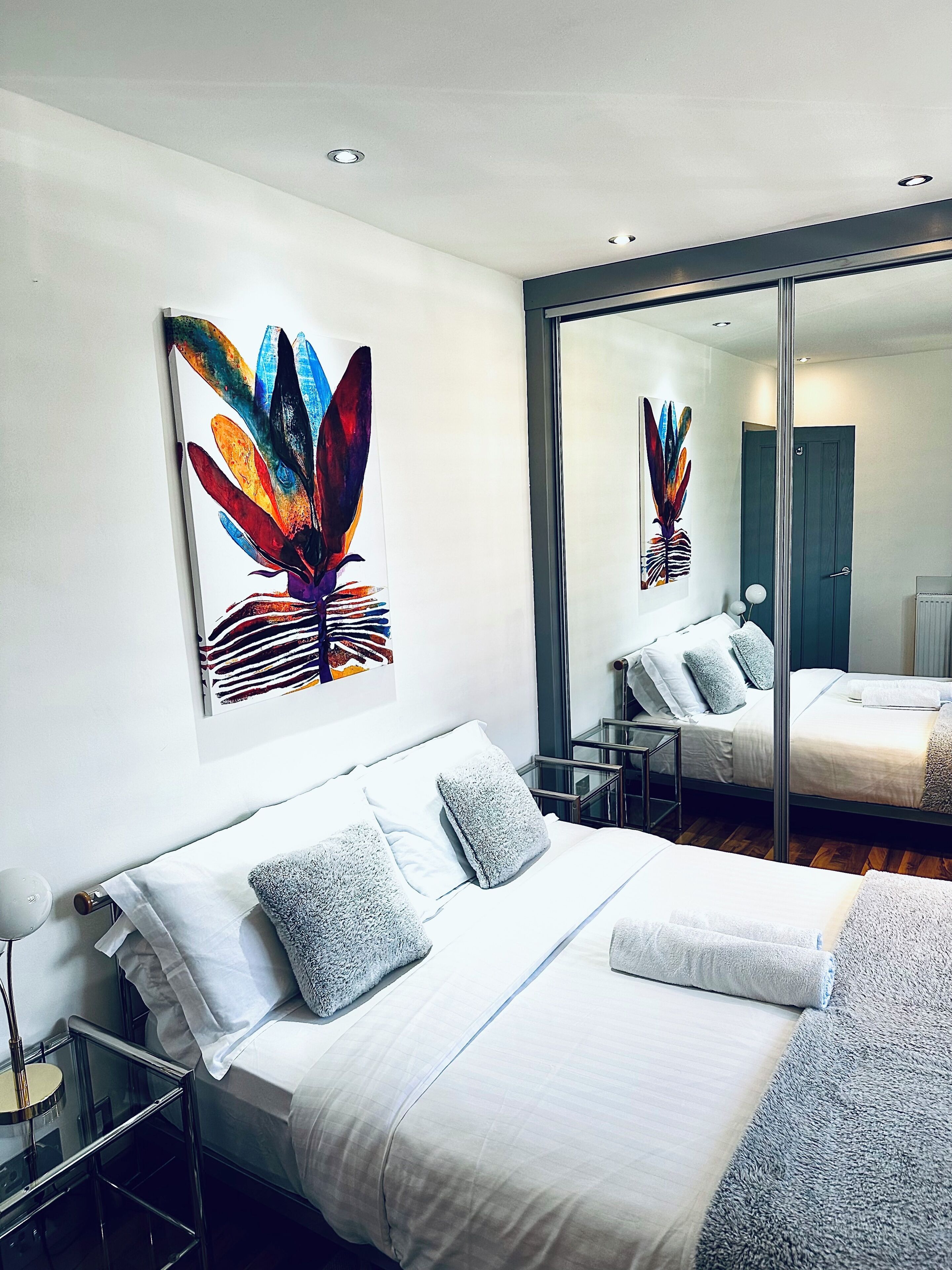 A modern hotel room with a large bed, a glass partition, and artwork on the wall.