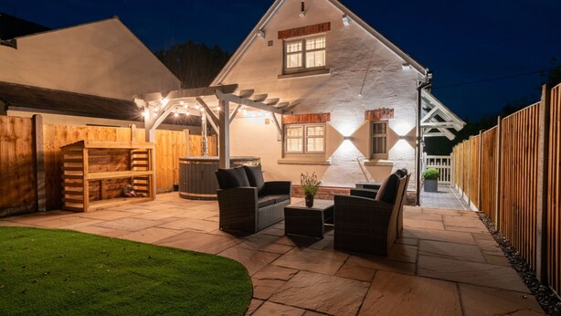 A stone house with a patio area featuring outdoor furniture and a hot tub. - Pilgrim Cottage - Luxury Cottages (Chester)