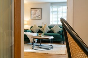 Un salon avec un canapé vert, deux coussins décoratifs, une table basse ronde et un tableau encadré au mur.