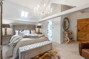 Une chambre spacieuse avec un grand lit, un lustre, une porte en bois et un miroir.