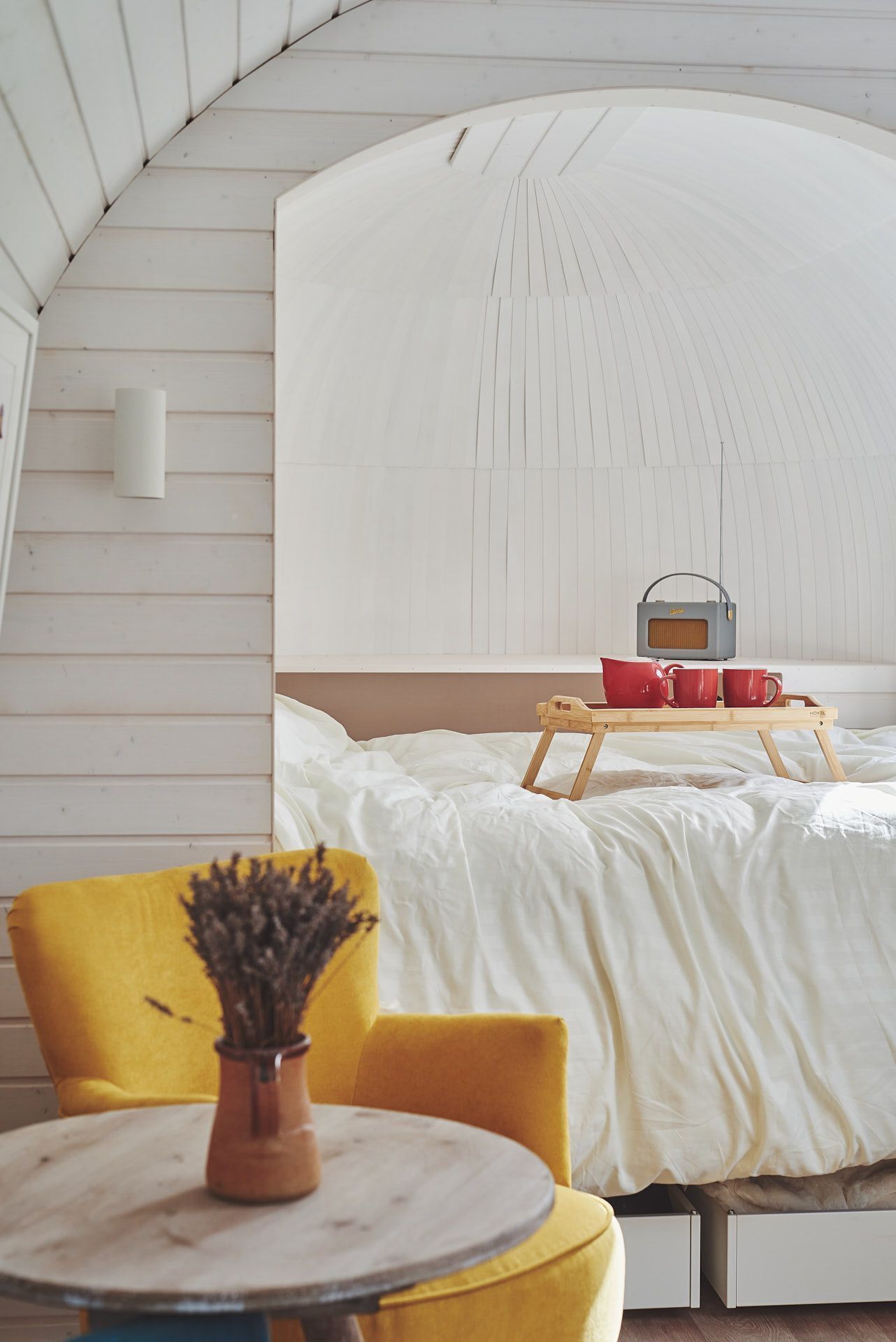 Een gezellige kamer met een bed, een houten nachtkastje, een gele stoel en een kleine tafel met een vaas.