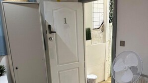 A white door with a number 1, a small trash bin, and a white radiator. - Studio Sleeps 3 - Outdoor Space - Pet Friendly (London)