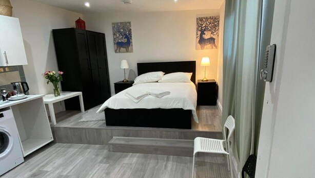 A modern hotel room with a bed, bedside tables, a desk, a washing machine, and artwork on the walls. - Studio Sleeps 3 - Outdoor Space - Pet Friendly (London)